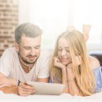 smiling-young-couple-lying-bed-looking-digital-tablet-bedroom_23-2147862772