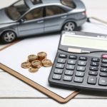 modelo-de-carro-calculadora-e-moedas-na-mesa-branca_1387-493