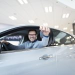 Happy buyer sitting in new vehicle and holding car keys.