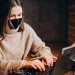 Young woman working on laptop in a cafe wearing mask
