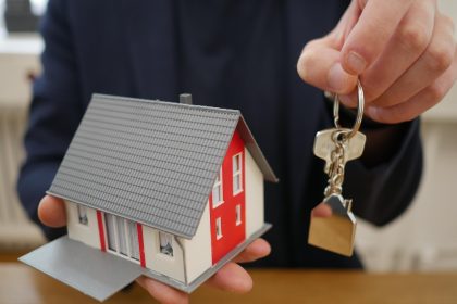 Mão segurando casa em miniatura e chaves, representando a compra de imóvel por consórcio