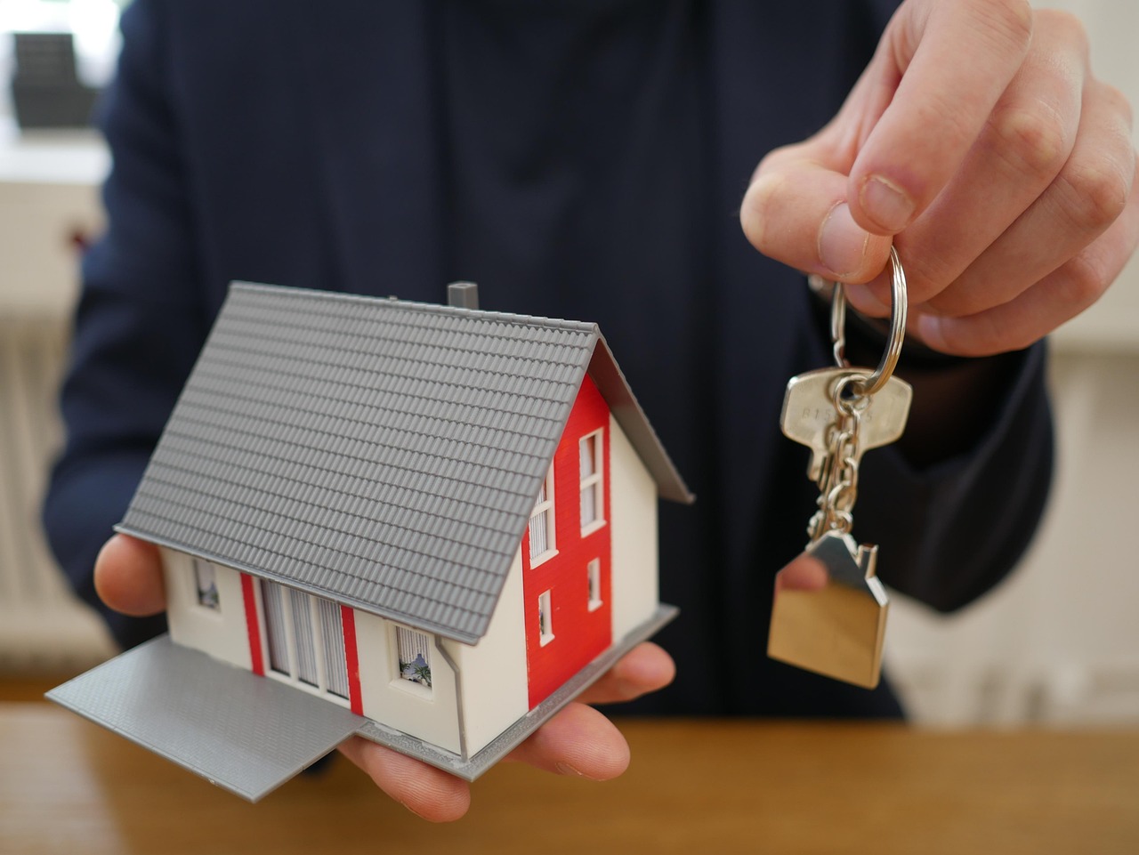 Mão segurando casa em miniatura e chaves, representando a compra de imóvel por consórcio